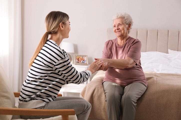 A young woman holds hands with an elderly woman, offering comfort.