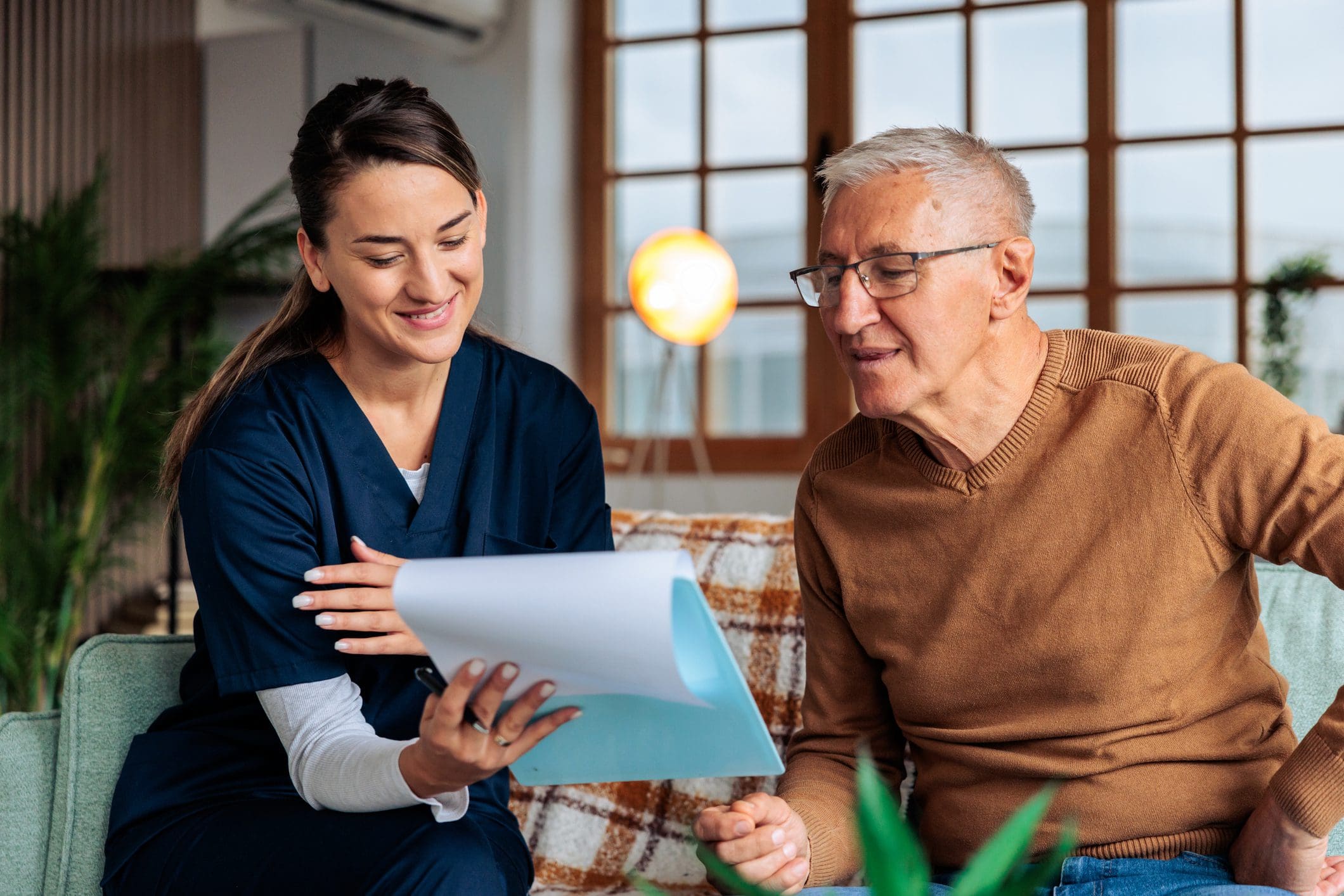 A nurse discussing a document with an elderly man in a cozy room.