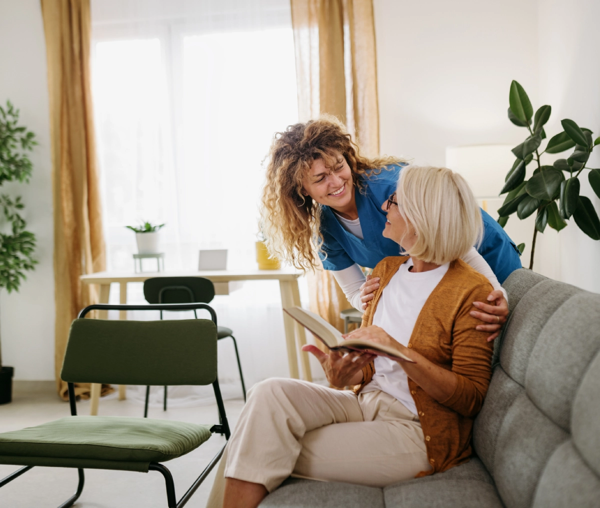 Two women sharing a joyful moment with a book on a couch.