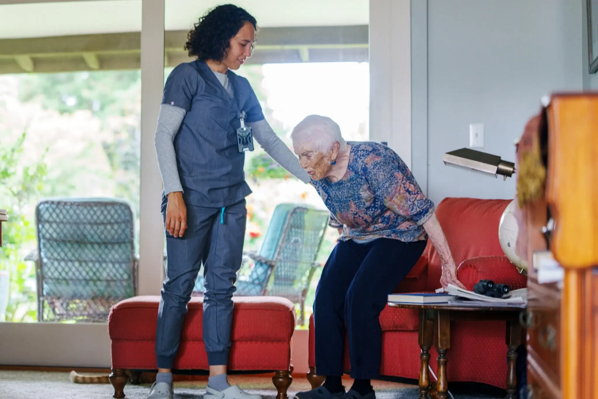 A nurse supports an elderly woman using a walker indoors.