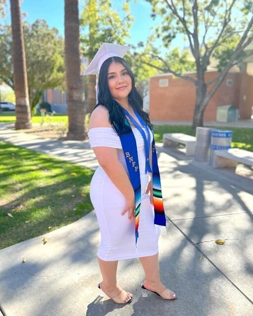 Graduate in white dress and cap outdoors
